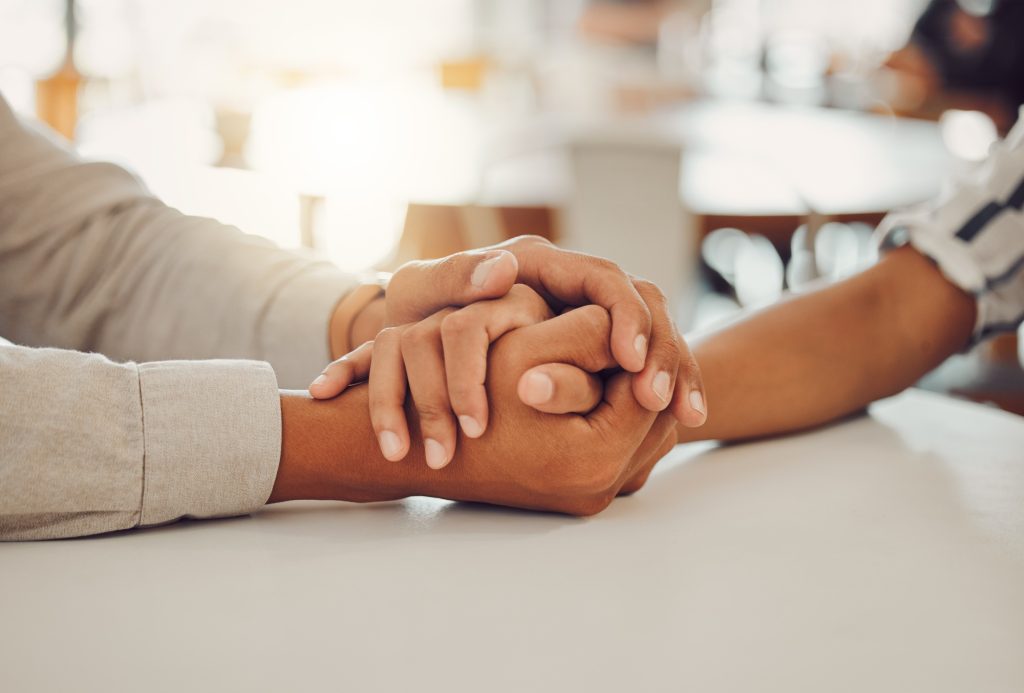 Close up of young man and woman holding hands at wooden table, from above. Loving couple expressing